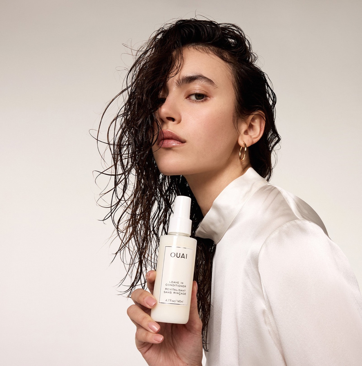 Ouai Leave In Conditioner held by a model with curly hair